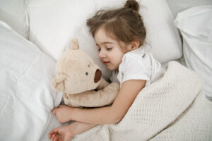 cute little girl is sleeping bed with teddy bear toy