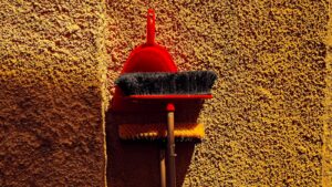 Red dustpan and broom leaning against wall